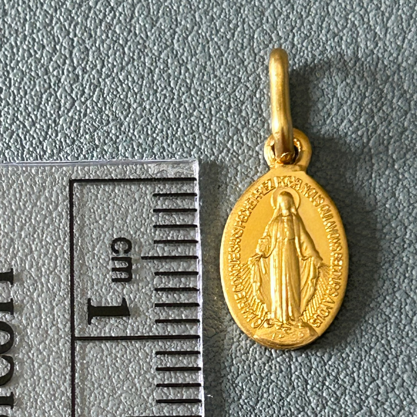 Gold pendant with a religious design next to a ruler for scale on a gray background