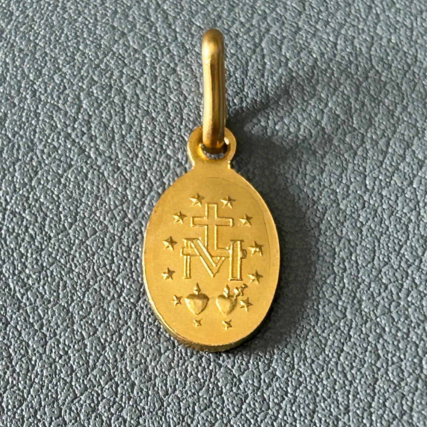 Gold pendant with religious symbols on a blue gray textured background